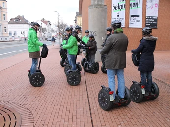 Segwaytour Herford-Pro Herford GmbH.JPG Gruppe von Menschen auf Segways bei einer geführten Tour durch ein städtisches Gebiet im Winter.