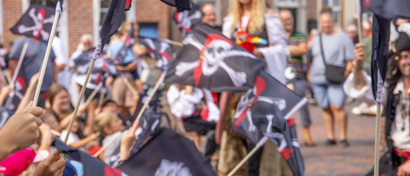 Greetsieler Piratenzauber Kinder schwenken Piratenflaggen bei einem fröhlichen Fest in Greetsiel mit verkleideten Piraten.