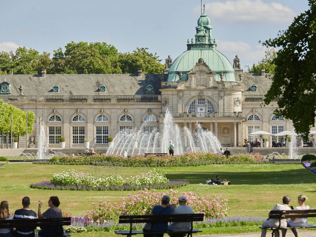 Barockes Gebäude mit Kuppel, Springbrunnen und Parkanlagen. Menschen auf Bänken genießen die Aussicht.