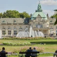 Barockes Gebäude mit Kuppel, Springbrunnen und Parkanlagen. Menschen auf Bänken genießen die Aussicht.