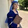 LAK: Almuth Cirksena Frau in königsblauem Mittelalterkleid mit Buch steht vor historischem Gebäude in Greetsiel.