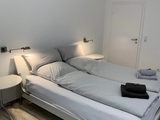 Schlafzimmer 1 Bild 7.jpg Zwei Einzelbetten mit hellgrauer Bettwäsche in einem modernen, minimalistisch eingerichteten Raum.