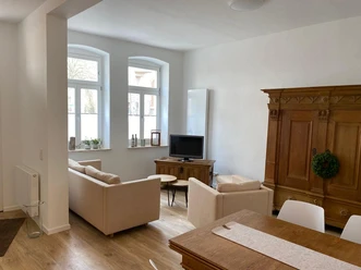 Wohn- Essbereich Bild 2.JPG Heller Wohn- und Essbereich mit beige Sofas, Holzschrank, Esstisch und großen Fenstern.