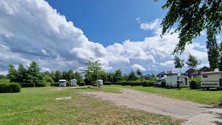 Wohnmobilstellplatz_Rhauderfehn_Ostfriesland Grüne Wiese mit geparkten Wohnmobilen unter einem weiten Himmel mit weißen Wolken.