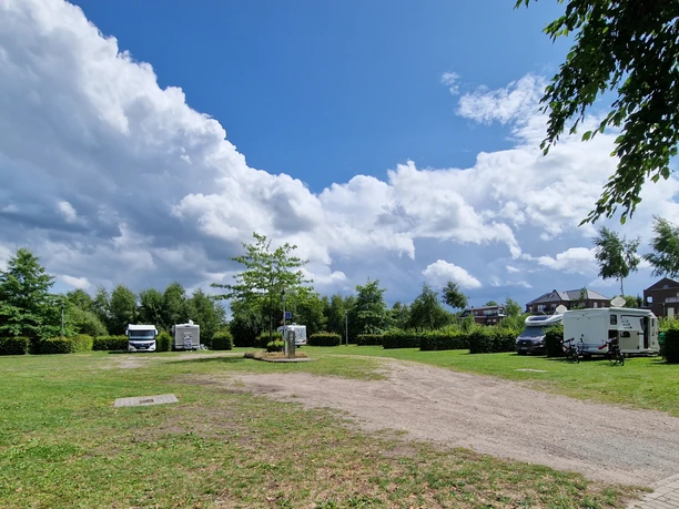 Wohnmobilstellplatz_Rhauderfehn_Ostfriesland Grüne Wiese mit geparkten Wohnmobilen unter einem weiten Himmel mit weißen Wolken.