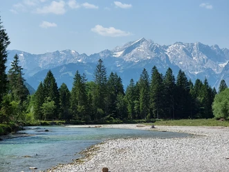 Loisach mit Blick auf die Alpspitze Klarer Fluss vor dichtem Nadelwald mit felsigen, teils verschneiten Bergen im Hintergrund