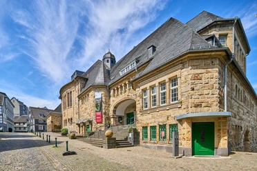 Historisches Bürgerhaus in Velbert-Langenberg Historisches Gebäude aus Sandstein mit markantem Schieferdach und grünen Türen in Velbert-Langenberg.