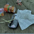 Wilder Müll PNG.PNG Verschiedene Abfälle, darunter Lebensmittelverpackungen und Plastikstraws, auf einem Holzboden verstreut.