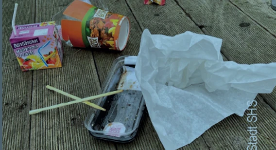 Wilder Müll PNG.PNG Verschiedene Abfälle, darunter Lebensmittelverpackungen und Plastikstraws, auf einem Holzboden verstreut.