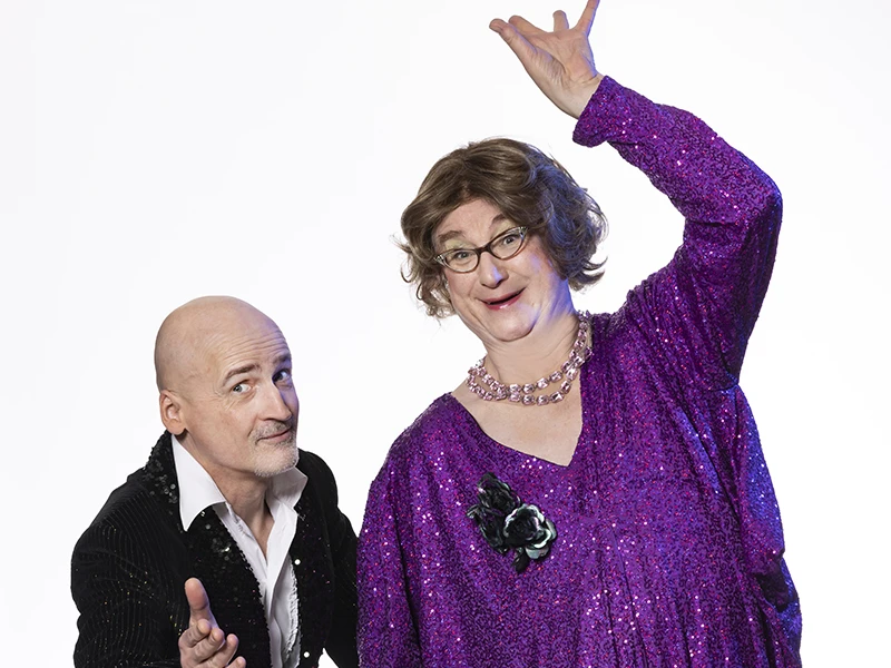 E&W by Paul Schimweg_0569_b_klein.jpg Zwei Menschen in festlicher Kleidung posieren freudig, wobei der Mann in einem glitzernden Anzug steht.