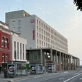 Paderborn Hauptbahnhof mit modernem Empfangsgebäude, Bahnhofsuhren und Werbeplakaten auf der Straße.