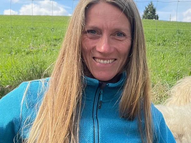 Miriam Mertens Eine Frau mit langen blonden Haaren und blauem Pullover lächelt vor einer grünen Wiese in die Kamera.