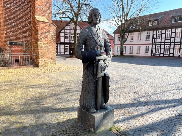 Die Statue des legendären Kriegers Widukind steht auf einem gepflasterten Platz, umringt von Fachwerkhäusern.