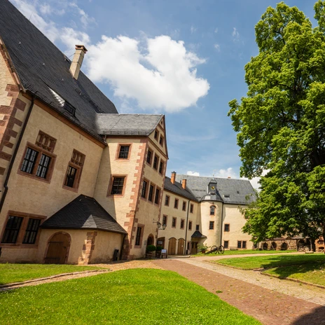 The inner courtyard of Mildenstein Castle has lush green grass, a large tree and walkways; Schlösserland, culture, sight, history, museum