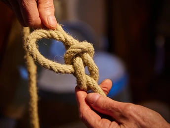 Heringsfängermuseum Ein Paar Hände zeigt das Knüpfen eines Knotens mit einem dicken Seil in einem Museum.