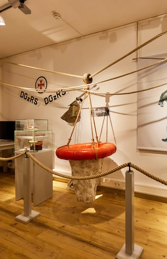 Heringsfängermuseum Ausstellungsraum im Heringsfängermuseum mit Rettungsring, Infotafel, Seilen und historischem Bild.