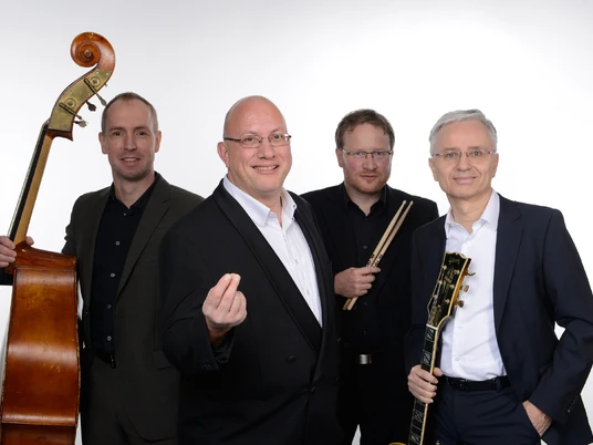 Jörg Hegemann Trio & Rolf Marx Vier Musiker in formeller Kleidung lächeln, mit Klavier, Gitarre, Kontrabass und Schlagzeug.