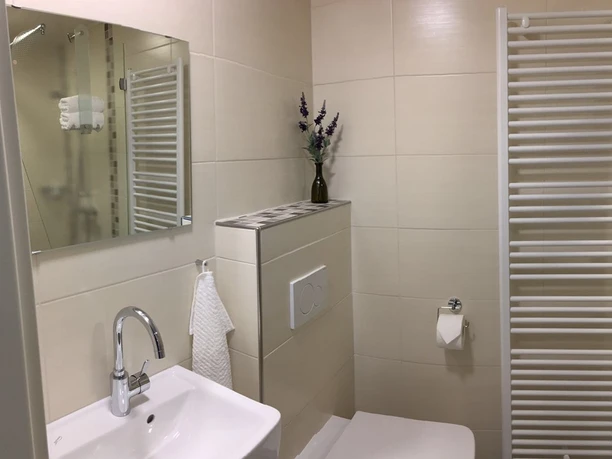 Bild2.jpg Ein helles, modernes Badezimmer mit weiß gefliesten Wänden, Handtuchheizung und elegantem Waschbecken.
