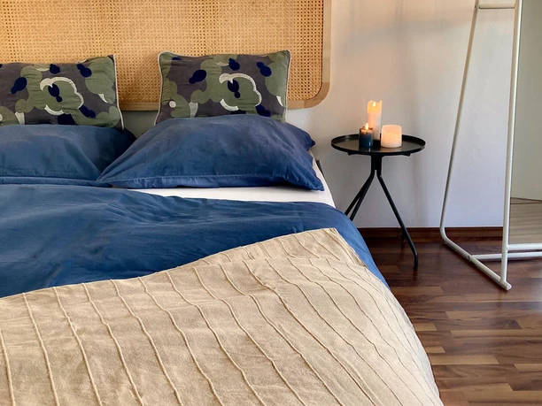 Schlafzimmer Senne Bungalow Ein gemütliches Schlafzimmer mit einem Doppelbett in Blautönen, Rattankopfteil und Kerzenakzenten.