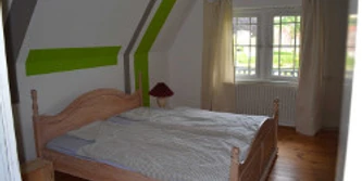 altstdtbhf-2.jpg Helles Schlafzimmer mit Holzfußboden, Dachschräge und Doppelbett. Fenster mit Blick ins Grüne.