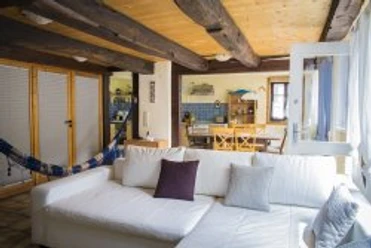 wohnraum1.jpg Wohnzimmer mit weißem Sofa, Holzbalkendecke und farbiger Küche im Hintergrund. Gemütliche Atmosphäre.