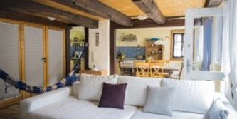 wohnraum1.jpg Wohnzimmer mit weißem Sofa, Holzbalkendecke und farbiger Küche im Hintergrund. Gemütliche Atmosphäre.