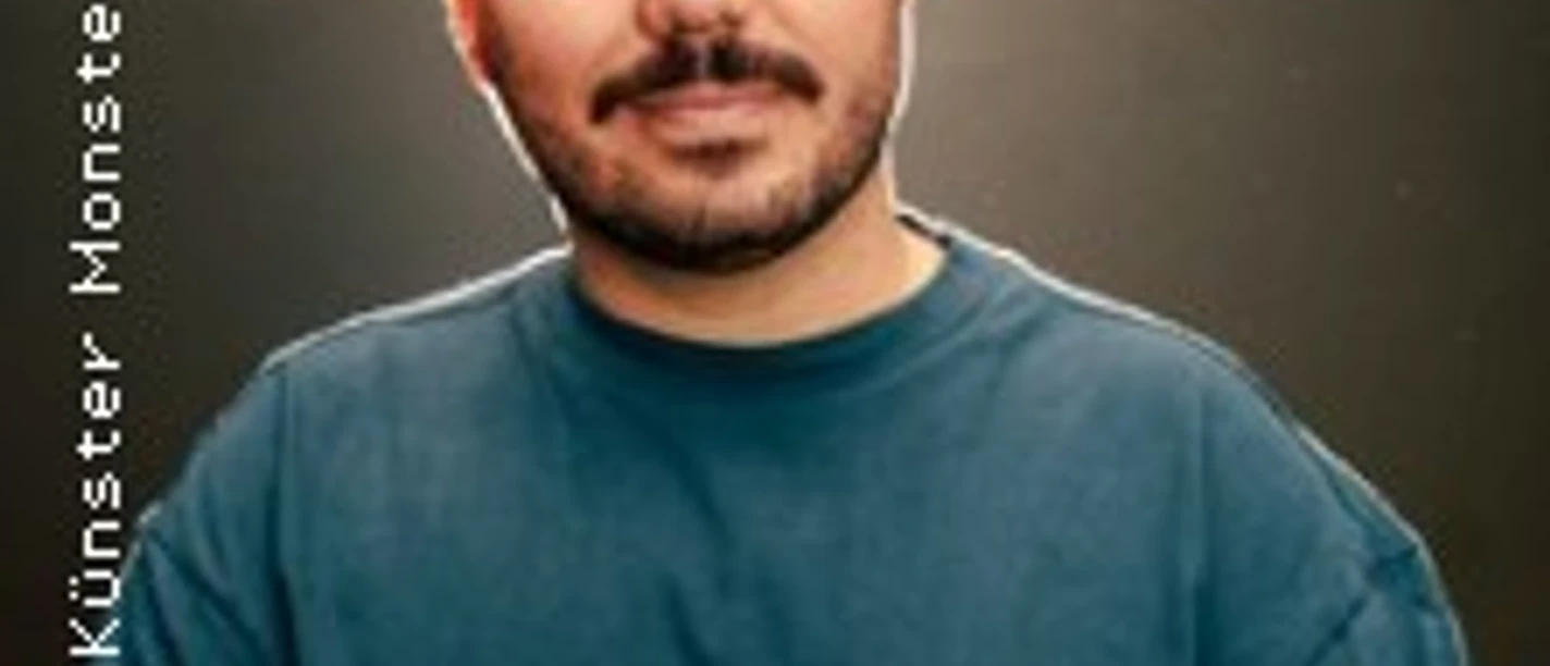 Porträt eines Mannes mit dunklem Haar und Bart in dunklem T-Shirt vor neutralem Hintergrund, freundlich blickend.