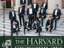 Eine Gruppe junger Männer in eleganten Anzügen steht lächelnd vor imposanten Säulen.