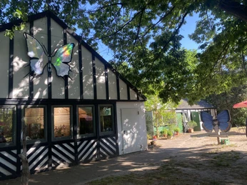 Außenansicht (c) ALARIS Schmetterlingspark Buchholz.jpg Der ALARIS Schmetterlingspark Buchholz zeigt eine charmante Fachwerkfassade mit großem Schmetterlingssymbol und umliegenden Bäumen.