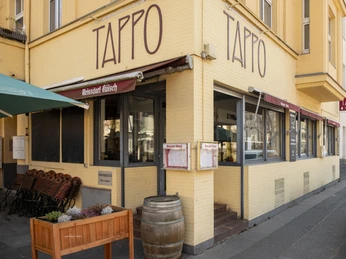 Tappo Gemütliches Restaurant „Tappo“ mit gelber Fassade und großen Fenstern an einer Straßenecke.Cozy "Tappo" restaurant with a yellow façade and large windows on a street corner.