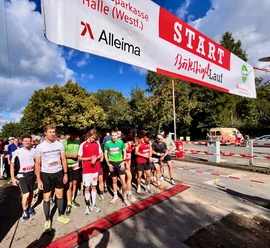 Läufergruppe unter rotem "Start"-Banner beim Brok(l)auf in Werther, sonniger Tag mit Bäumen im Hintergrund.