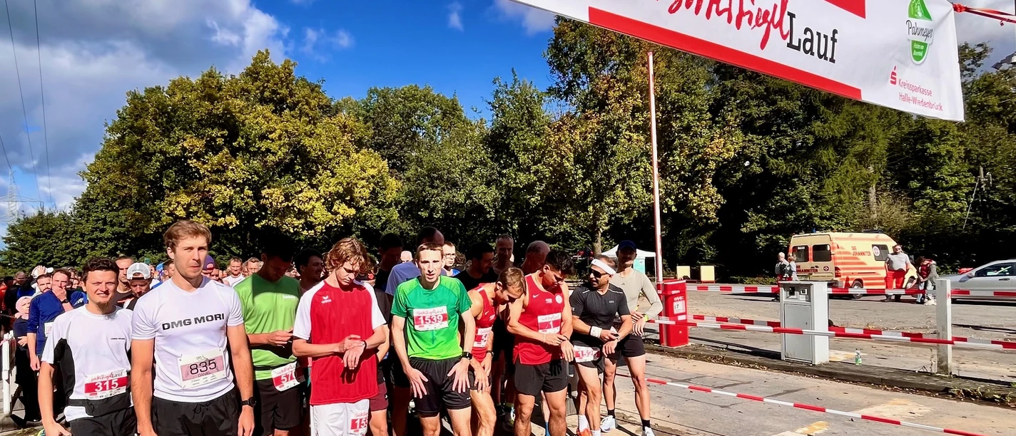 Läufergruppe unter rotem "Start"-Banner beim Brok(l)auf in Werther, sonniger Tag mit Bäumen im Hintergrund.