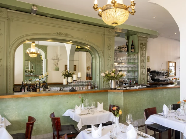 Restaurant Der vierte König A stylishly furnished dining room with green wall paneling and elegantly laid tables.