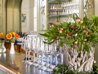 Restaurant Der vierte König Auf einem stilvoll gestaltetem Tresen steht ein Arrangement aus grünen Pflanzen und Blumen vor eleganter, klassischer Holztäfelung.An arrangement of green plants and flowers stands on a stylishly designed counter in front of elegant, classic wood paneling.