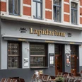 Lapidarium Ein Eingang des Lapidarium in Köln mit roten Ziegeln und blauen Fensterrahmen.Facade of a historic pub named "Lapidarium" with outdoor seating and brick architecture.