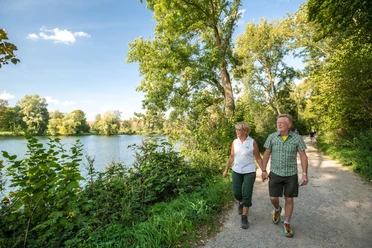Wandern entlang des Abtskücher Teiches in Heiligenhaus Paar beim Wandern auf einem sonnigen Pfad am Abtskücher Teich, Heiligenhaus, umgeben von Bäumen.