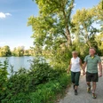 Wandern entlang des Abtskücher Teiches in Heiligenhaus Paar beim Wandern auf einem sonnigen Pfad am Abtskücher Teich, Heiligenhaus, umgeben von Bäumen.