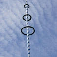 Blau-weiß gestreifter Maibaum ragt in den bewölkten Himmel, geschmückt mit grünen Ringen.