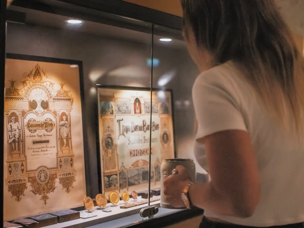 Braukeller Frau mit Bierkrug vor einer Vitrinenscheibe.