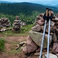 Nordic Walking Nordic-Walking-Stöcke lehnen an einem Steinhaufen vor einem Hintergrund aus bewaldeten Berghängen.