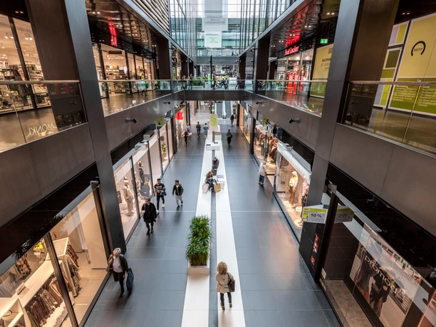 Pohled na dvoupatrové nákupní centrum s mnoha obchody, návštěvníky, nákupními a volnočasovými aktivitami