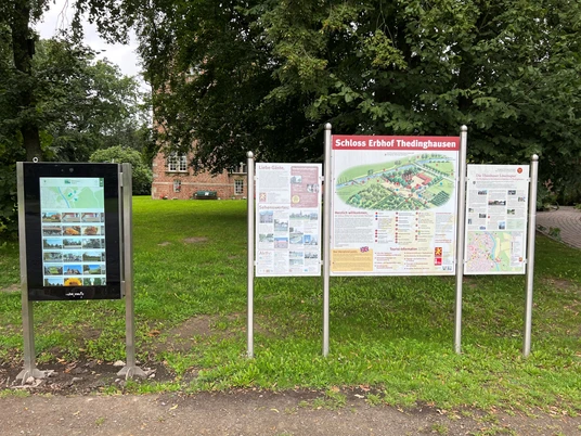 Infoterminal am Schloss Erbhof Infoterminal und Schautafeln vor Schloss Erbhof, umgeben von grünen Bäumen und historischen Mauern.