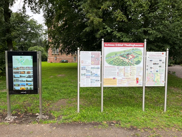 Infoterminal am Schloss Erbhof Infoterminal und Schautafeln vor Schloss Erbhof, umgeben von grünen Bäumen und historischen Mauern.