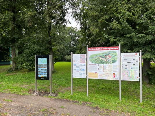 Infoterminal am Schloss Erbhof Infoterminal und Schautafeln des Schlosses Erbhof umgeben von Bäumen auf einer grünen Wiese.