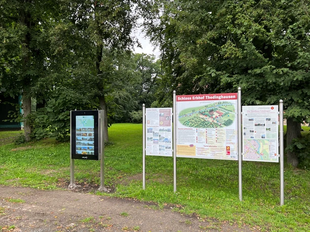 Infoterminal am Schloss Erbhof Infoterminal und Schautafeln des Schlosses Erbhof umgeben von Bäumen auf einer grünen Wiese.