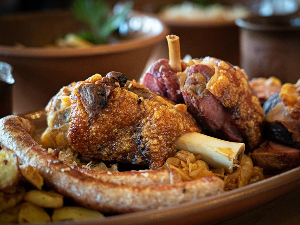 Haxenhaus A rustic platter with a crispy pork knuckle, sausages, potatoes, and cabbage on a wooden table.