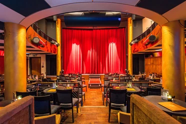 Varietésaal im Krystallpalast Varieté Leipzig - Abendveranstaltungen in Leipzig Blick auf die Bühne mit rotem Vorhang im Varietésaal des Krystallpalast Varieté Leipzig mit zahlreichen Stühlen und Tischen bei heller Beleuchtung, Kultur, Abendveranstaltung