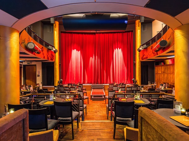 Varietésaal im Krystallpalast Varieté Leipzig - Abendveranstaltungen in Leipzig Blick auf die Bühne mit rotem Vorhang im Varietésaal des Krystallpalast Varieté Leipzig mit zahlreichen Stühlen und Tischen bei heller Beleuchtung, Kultur, Abendveranstaltung