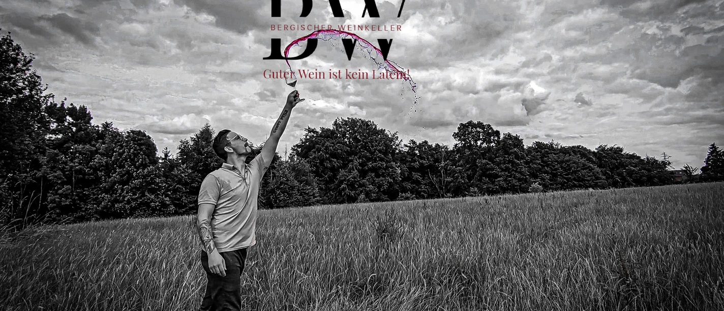 Bergischer Weinkeller Ein Mann in einem Feld wirft ein Weinglas in die Luft, umgeben von Bäumen und bewölktem Himmel.