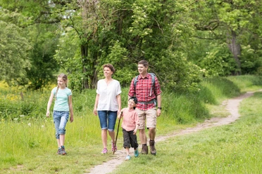 Wandern mit der Familie auf dem neanderland STEIG Familie wandert lächelnd zusammen auf einem schmalen Pfad inmitten grüner Natur im neanderland STEIG.